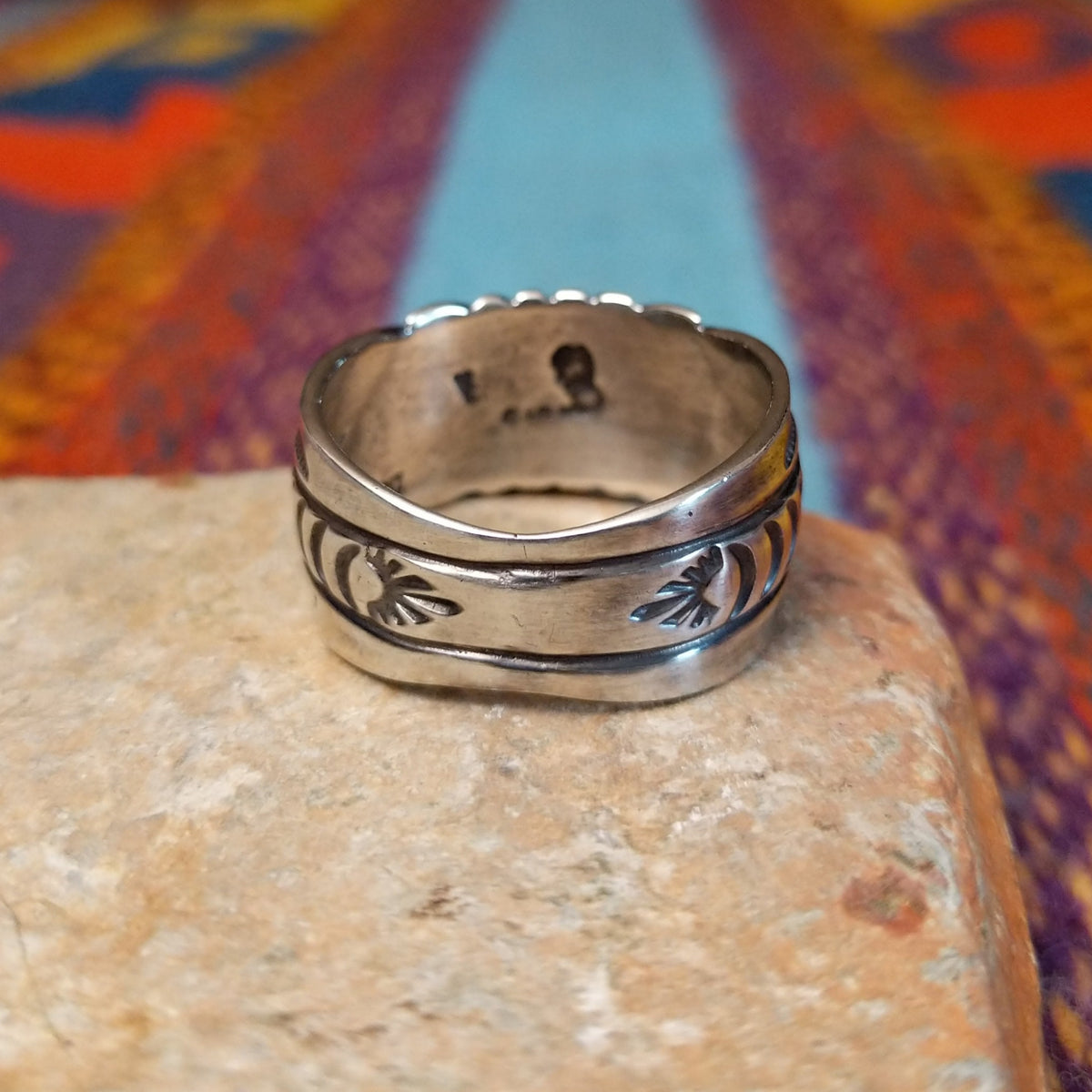 Turquoise Ring by Raymond Coriz featuring a round bright-blue turquoise cabochon centered on a wide silver band with hand-stamped curved and sunburst designs; underside view.