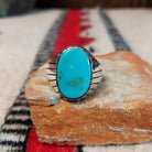 Turquoise ring by Rex Abeita featuring a large oval blue-green turquoise stone with natural matrix, set in silver with bold geometric line detailing along the sides.