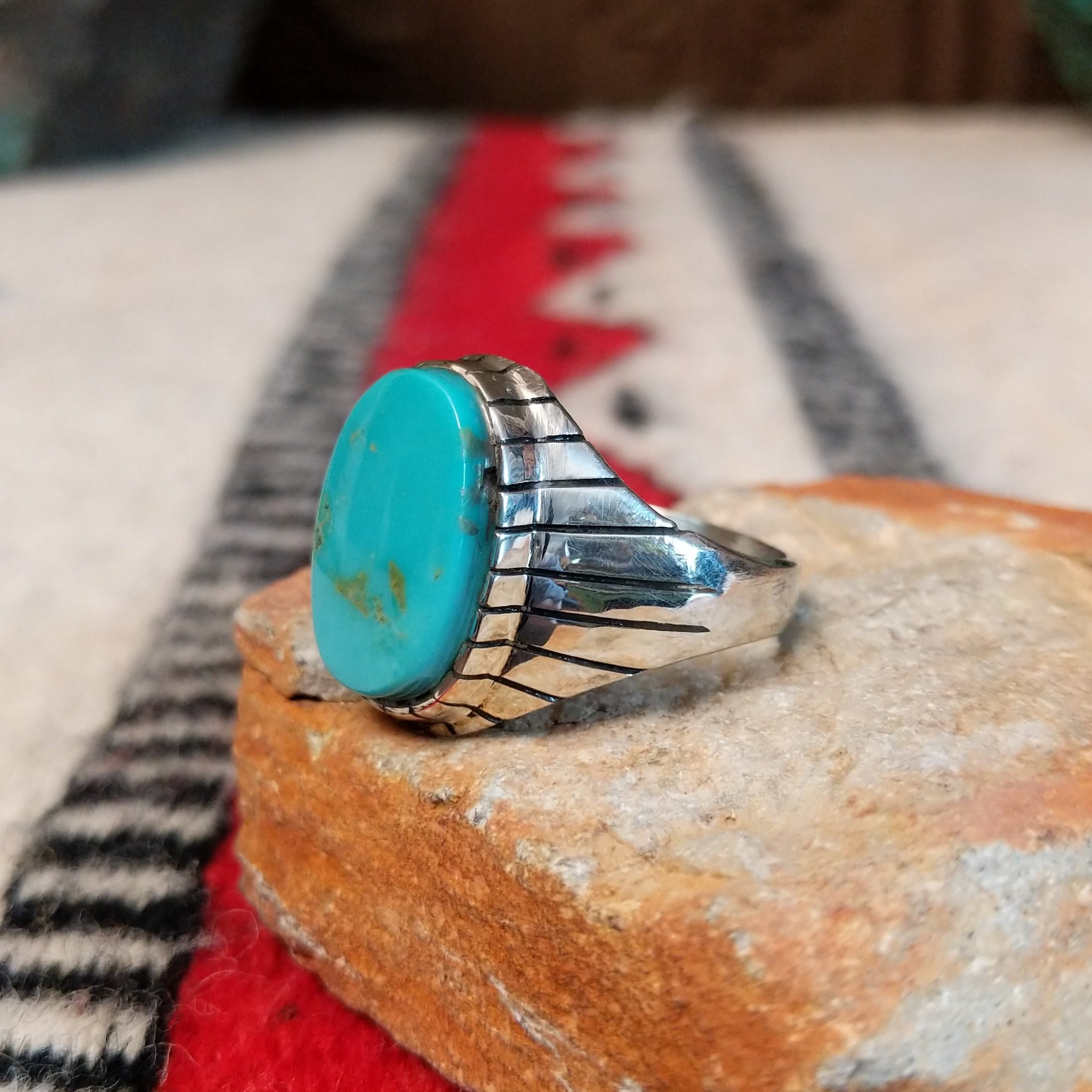 Turquoise ring by Rex Abeita featuring a large oval blue-green turquoise stone with natural matrix, set in silver with bold geometric line detailing along the sides; side view.