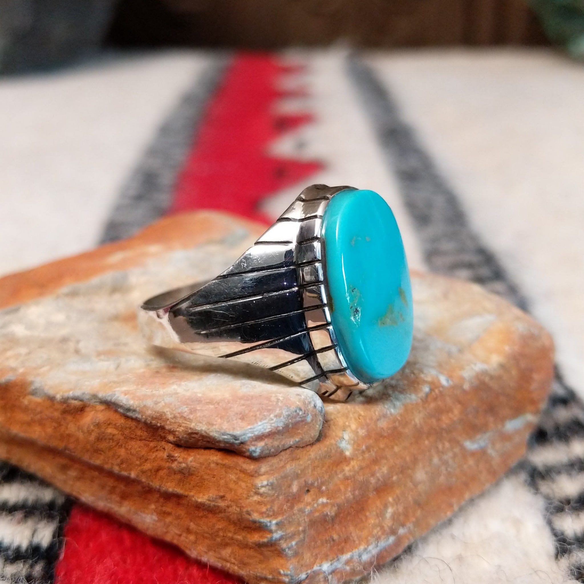 Turquoise ring by Rex Abeita featuring a large oval blue-green turquoise stone with natural matrix, set in silver with bold geometric line detailing along the sides; side view.