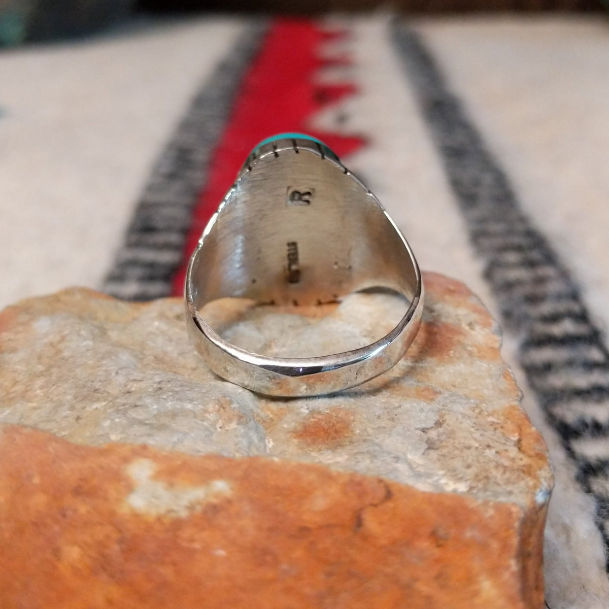 Turquoise ring by Rex Abeita featuring a large oval blue-green turquoise stone with natural matrix, set in silver with bold geometric line detailing along the sides; underside view.