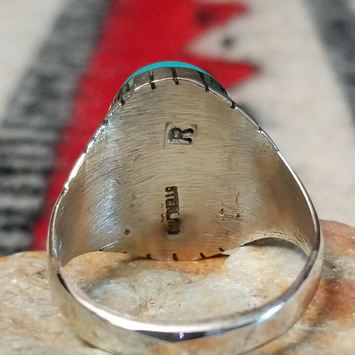 Turquoise ring by Rex Abeita featuring a large oval blue-green turquoise stone with natural matrix, set in silver with bold geometric line detailing along the sides; artisan and Sterling Silver stamp.