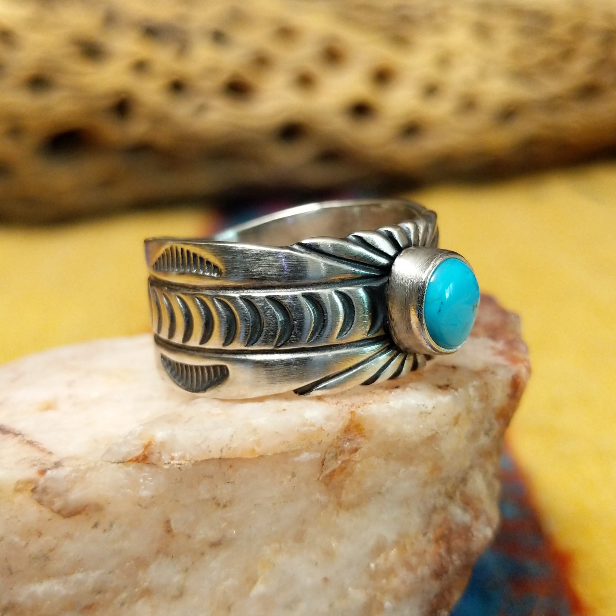 Turquoise round ring by Raymond Coriz, featuring a round turquoise stone set in a handcrafted sterling silver ring with an intricately detailed hand-stamped band.  Side view.