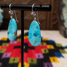 Turquoise Slab Earrings by Ronald Chavez featuring elongated freeform blue turquoise stones with natural tan, brown, and dark matrix, suspended from silver-tone hooks; side view.
