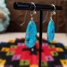 Turquoise Slab Earrings by Ronald Chavez featuring elongated freeform blue turquoise stones with natural tan, brown, and dark matrix, suspended from silver-tone hooks; side view.