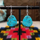 Turquoise Slab Earrings by Ronald Chavez featuring polished freeform blue turquoise stones with natural brown, gray, and green matrix, suspended from simple silver-tone hooks.
