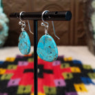 Turquoise Slab Earrings by Ronald Chavez featuring polished freeform blue turquoise stones with natural brown, gray, and green matrix, suspended from simple silver-tone hooks; side view.