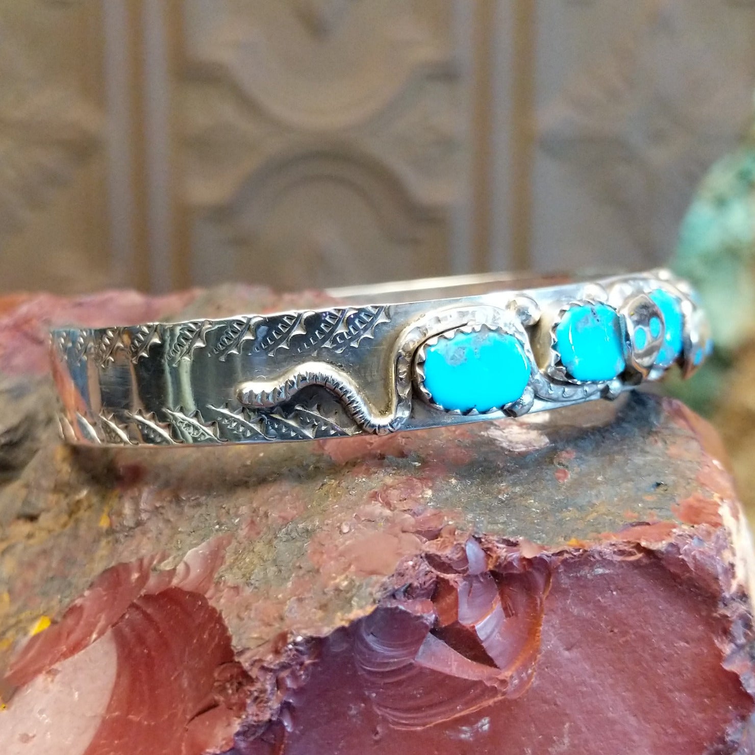 Sterling silver cuff bracelet with turquoise set in notched bezels and silverwork formed as a snake along the surface.