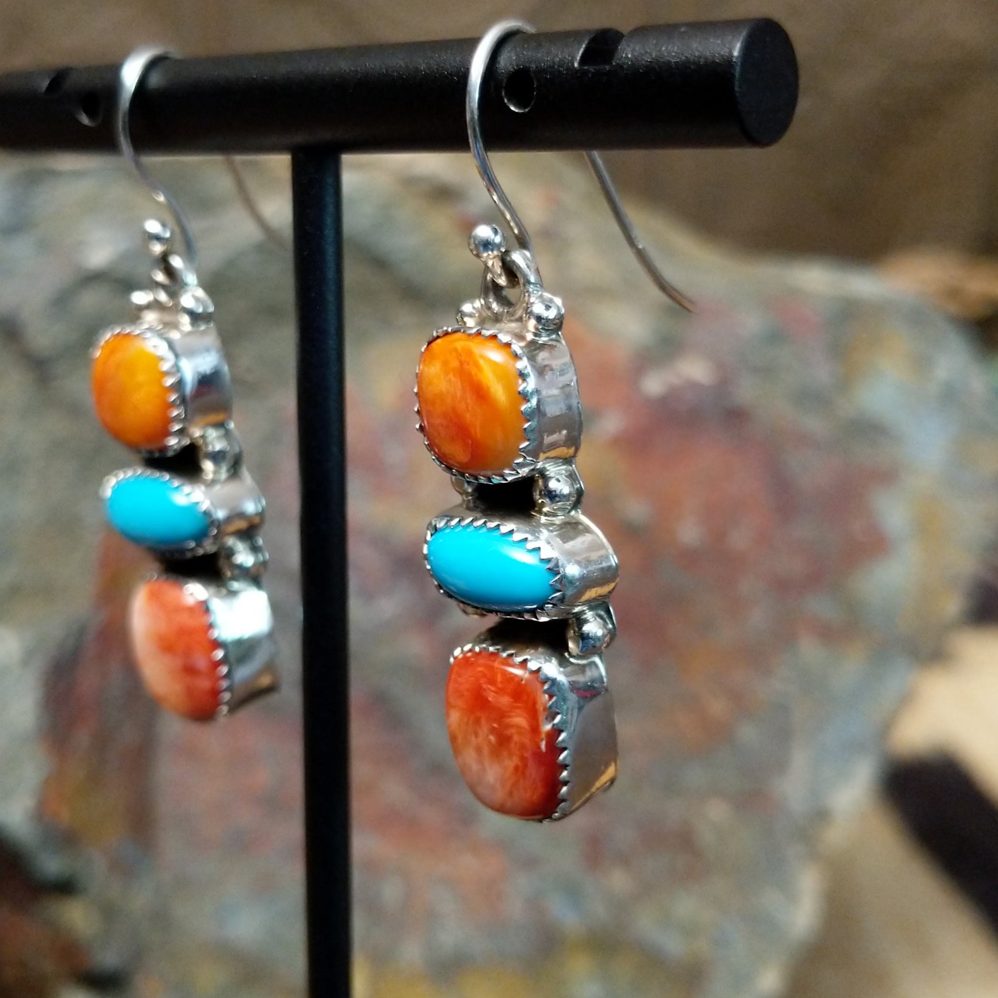 Handcrafted sterling silver turquoise and spiny oyster earrings by the Platero Family, featuring a three-stone dangle design with vibrant orange and blue gemstones; side view.