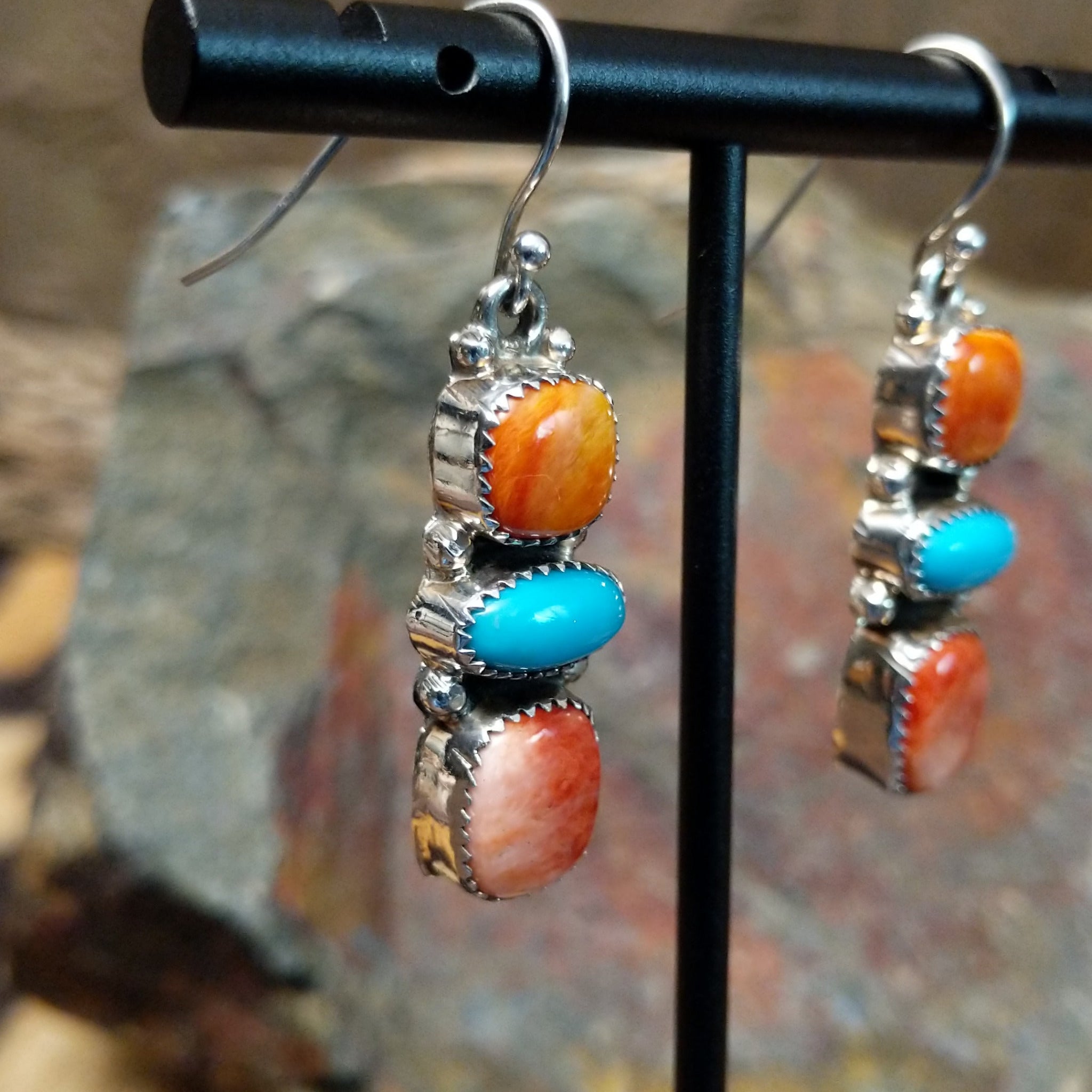 Handcrafted sterling silver turquoise and spiny oyster earrings by the Platero Family, featuring a three-stone dangle design with vibrant orange and blue gemstones; side view.