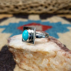 Turquoise square ring by Ann Curley, featuring a vibrant square turquoise stone with natural blue tones and matrix set in a handcrafted sterling silver band.  Side view.