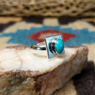 Turquoise square ring by Ann Curley, featuring a vibrant square turquoise stone with natural blue tones and matrix set in a handcrafted sterling silver band.  Side view.