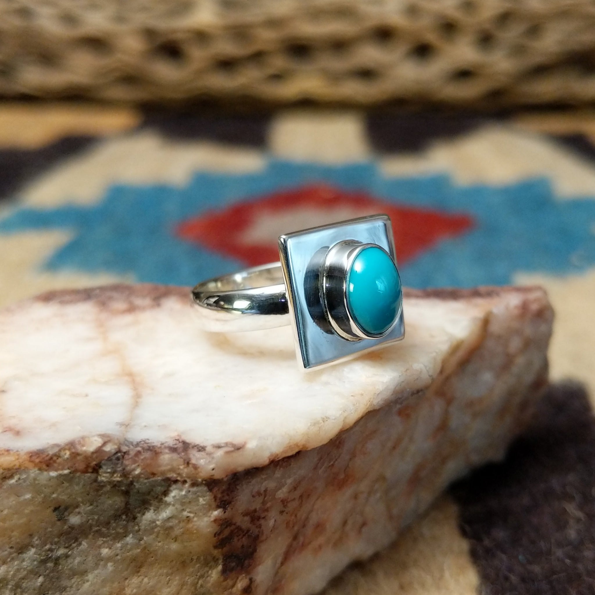 Turquoise square ring by Ann Curley, featuring a vibrant square turquoise stone with natural blue tones and matrix set in a handcrafted sterling silver band.  Side view.