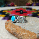 Radiant Turquoise Ring by Angela Martin featuring a round sky-blue turquoise stone set in sterling silver with flowing wave-like silver strands; side view.