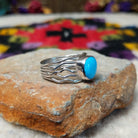 Radiant Turquoise Ring by Angela Martin featuring a round sky-blue turquoise stone set in sterling silver with flowing wave-like silver strands; side view.
