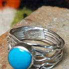 Radiant Turquoise Ring by Angela Martin featuring a round sky-blue turquoise stone set in sterling silver with flowing wave-like silver strands; artisan and Sterling Silver stamp.