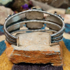 Handcrafted sterling silver cuff by Linda Johnson featuring three vibrant turquoise cabochons with twisted rope bezels, ornate silver beadwork, and a classic double-wire cuff design; underside view.