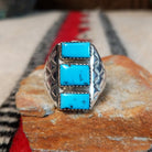 Turquoise Trio Ring by Pauline Nelson featuring three rectangular blue turquoise stones arranged vertically in serrated silver bezels, with detailed hand-stamped designs along the wide silver band.