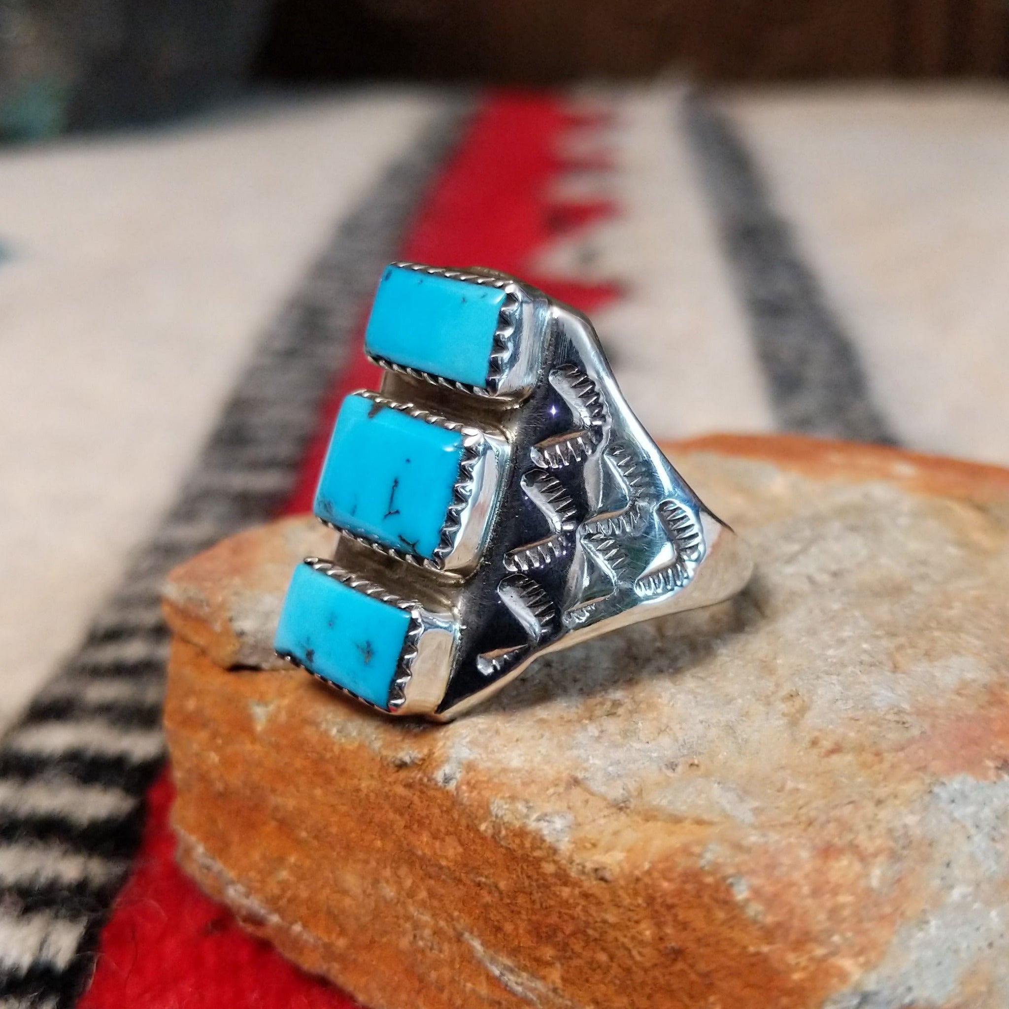 Turquoise Trio Ring by Pauline Nelson featuring three rectangular blue turquoise stones arranged vertically in serrated silver bezels, with detailed hand-stamped designs along the wide silver band; side view.