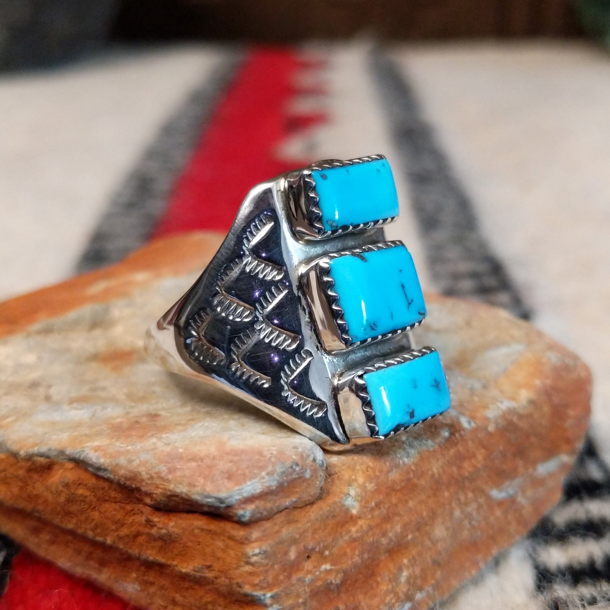 Turquoise Trio Ring by Pauline Nelson featuring three rectangular blue turquoise stones arranged vertically in serrated silver bezels, with detailed hand-stamped designs along the wide silver band; side view.