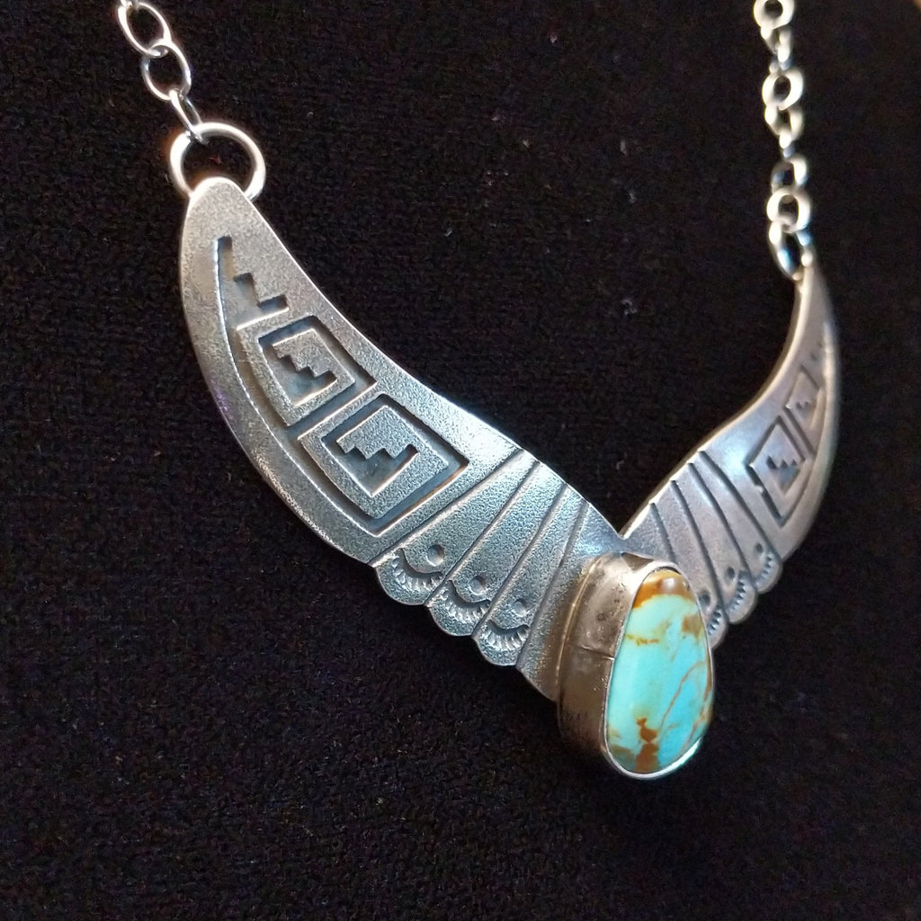 Turquoise centerpiece with sterling silver wings featuring stamped detailing, connected by the chain of the necklace.