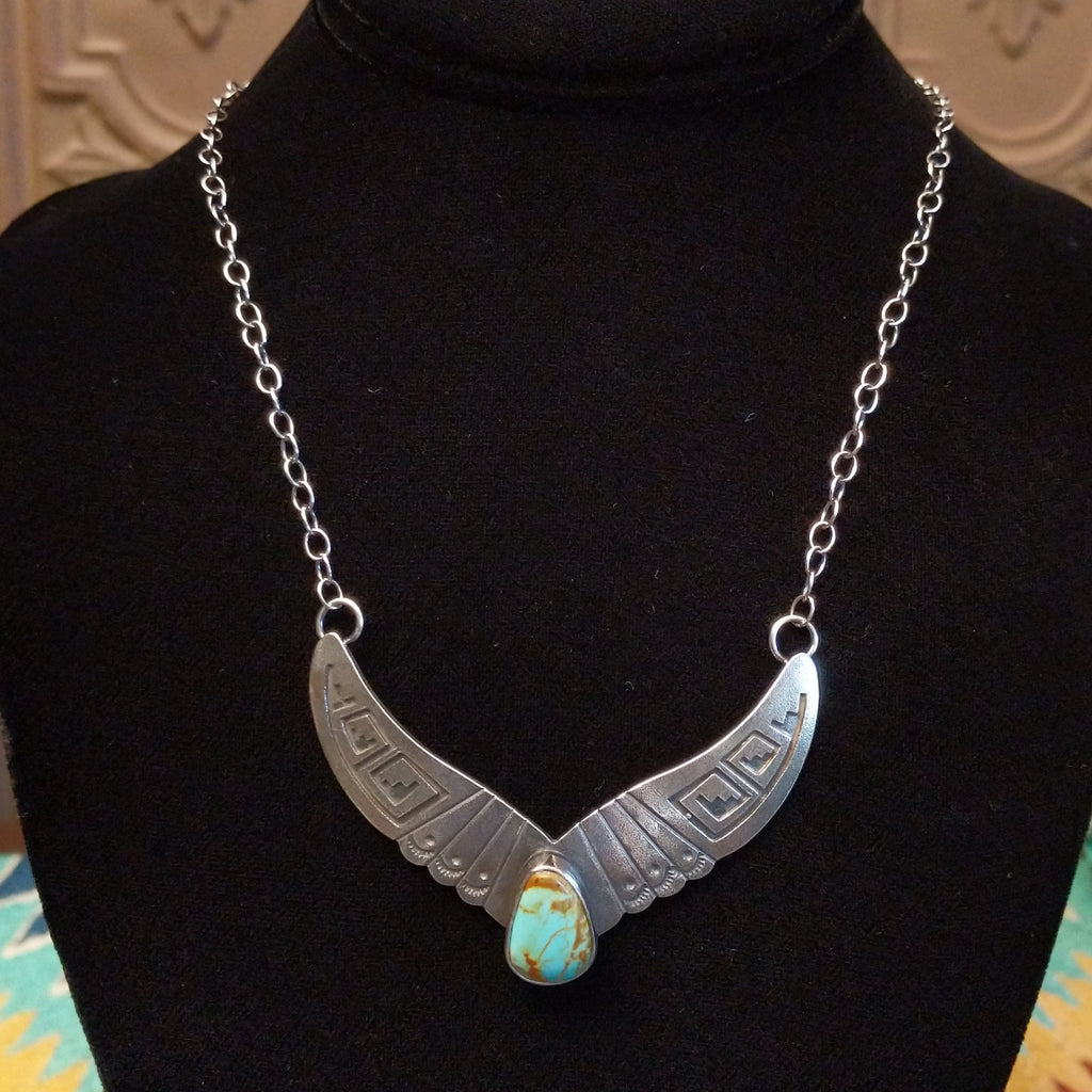Turquoise centerpiece with sterling silver wings featuring stamped detailing, connected by the chain of the necklace.