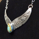 Turquoise centerpiece with sterling silver wings featuring stamped detailing, connected by the chain of the necklace.