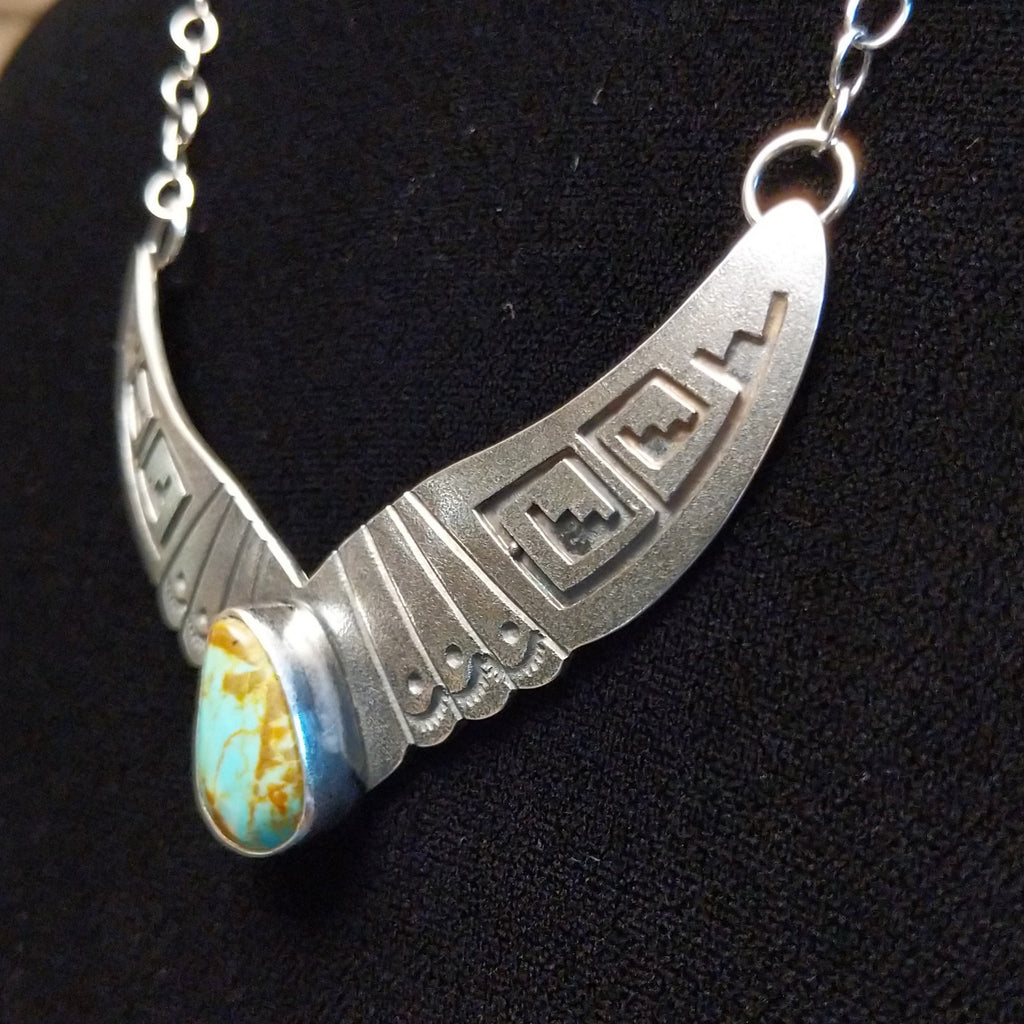 Turquoise centerpiece with sterling silver wings featuring stamped detailing, connected by the chain of the necklace.