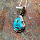 Handcrafted sterling silver turquoise pendant by Elgin Hoskey, featuring a natural blue turquoise stone with brown matrix in a smooth freeform setting; side view.