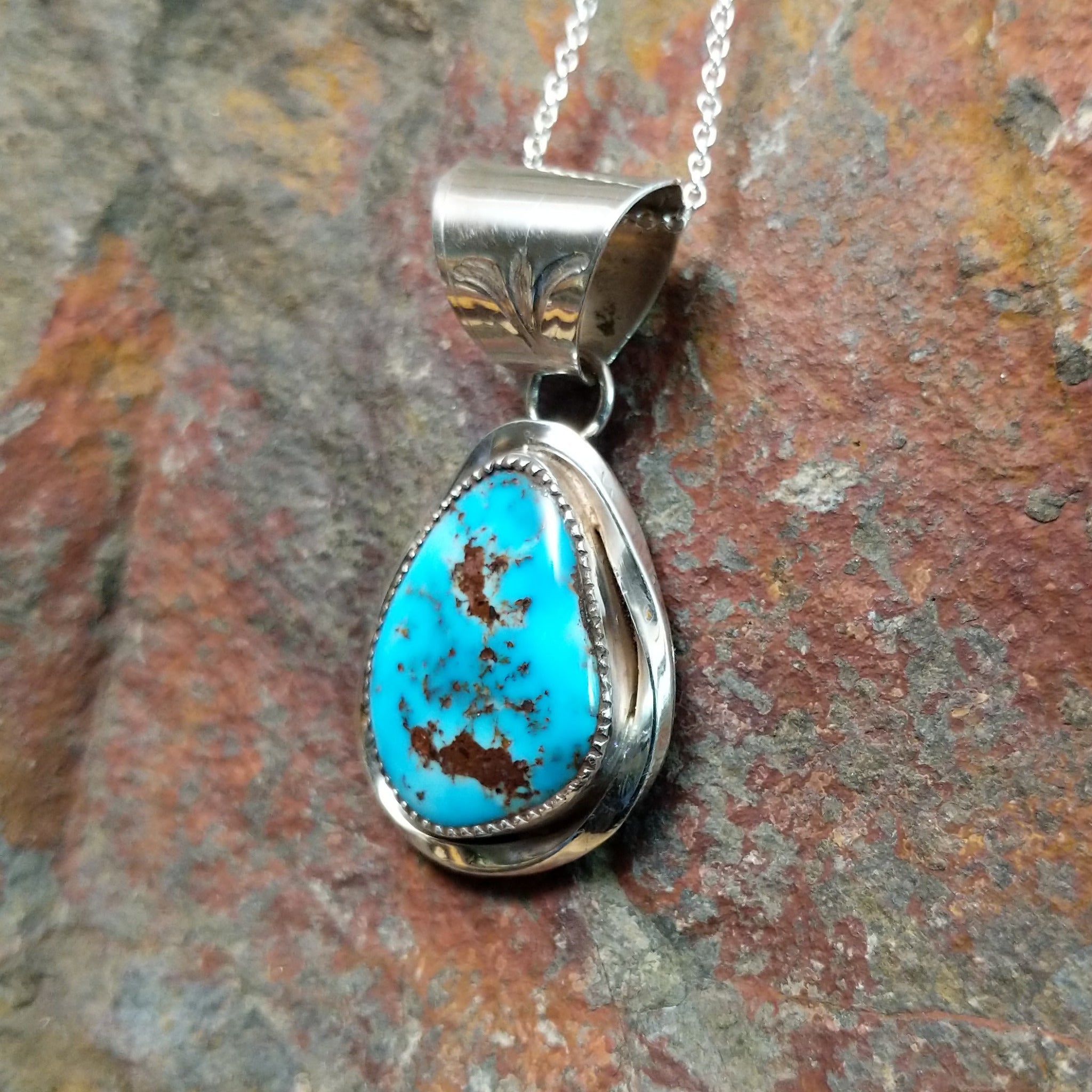 Handcrafted sterling silver turquoise pendant by Elgin Hoskey, featuring a natural blue turquoise stone with brown matrix in a smooth freeform setting; side view.