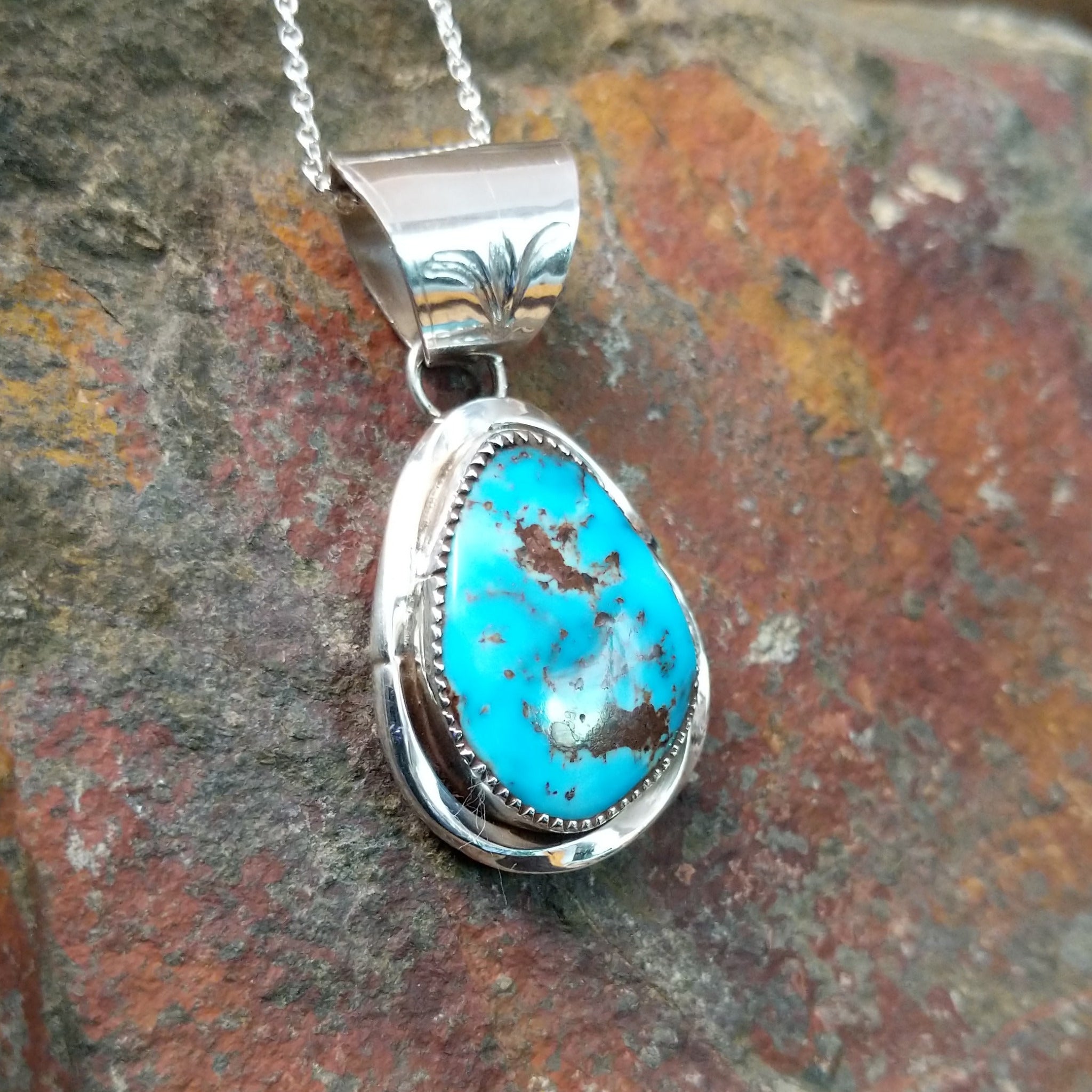 Handcrafted sterling silver turquoise pendant by Elgin Hoskey, featuring a natural blue turquoise stone with brown matrix in a smooth freeform setting; side view.