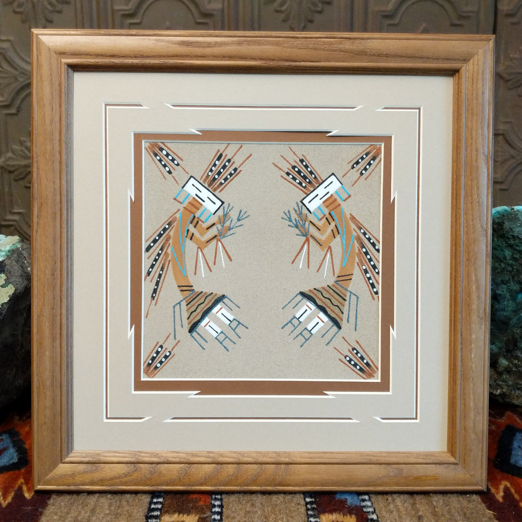 Sand depicting two Yei dancers set within a wooden frame.