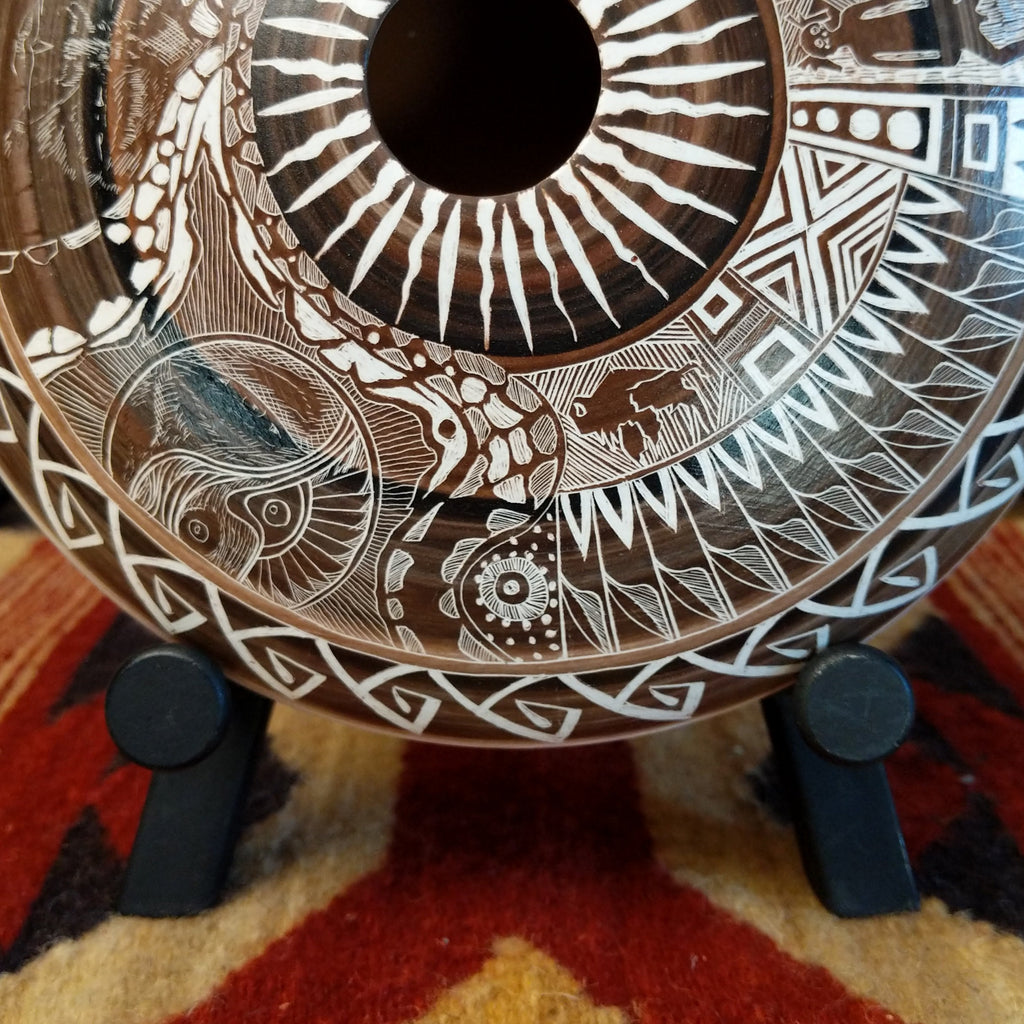 Decorative pottery with intricate white patterns on a stand against a colorful background