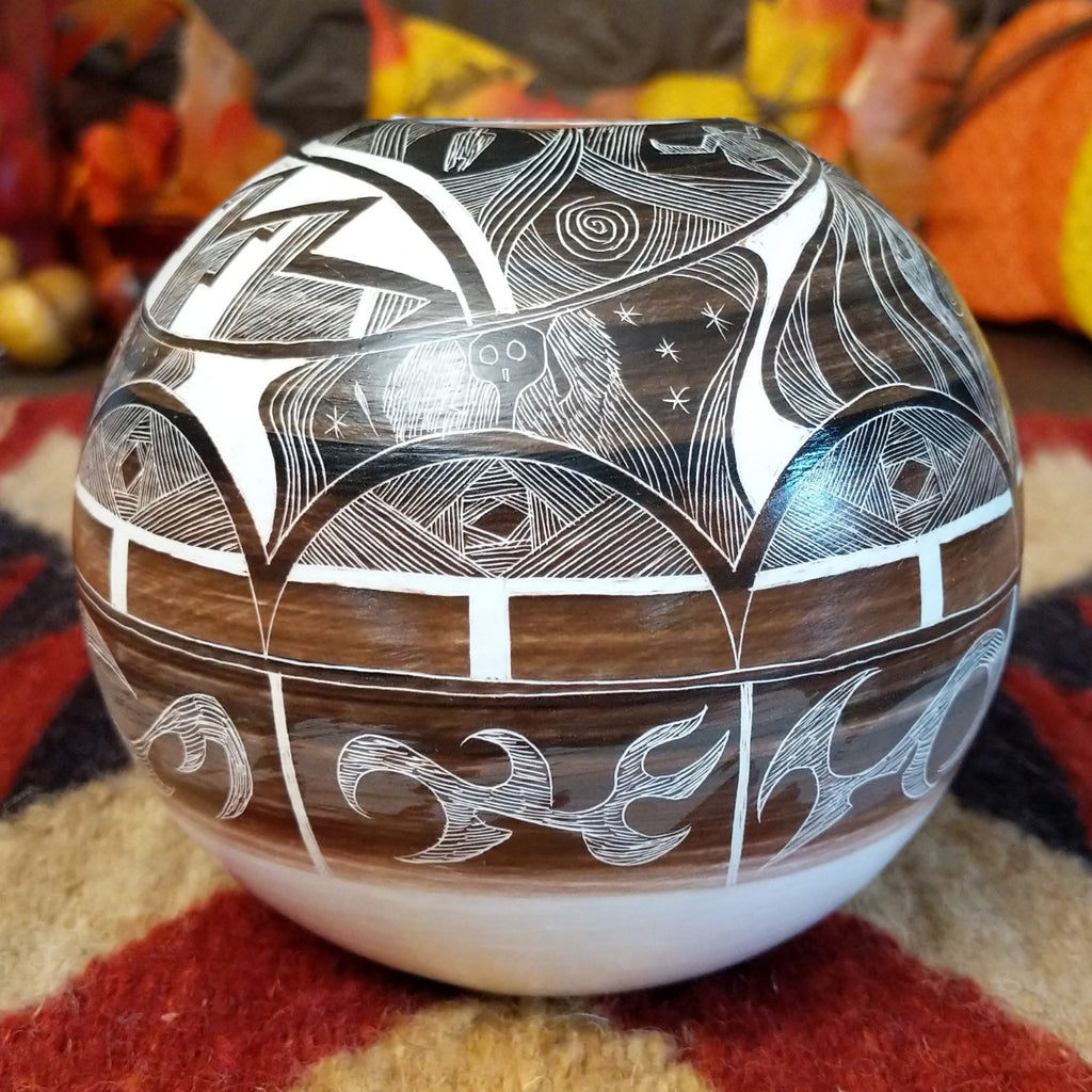 White clay with brown accents creating a pottery piece with intricately carved designs all along the surface.