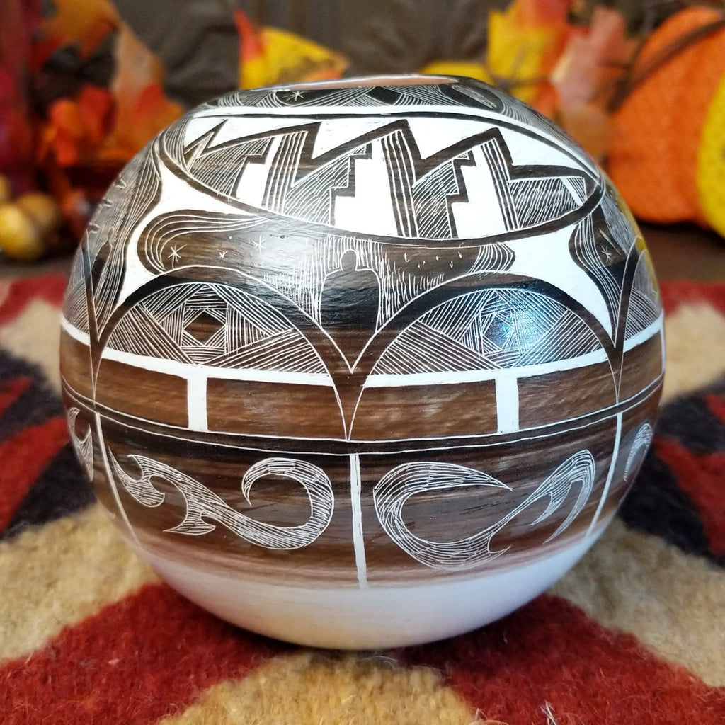 White clay with brown accents creating a pottery piece with intricately carved designs all along the surface.