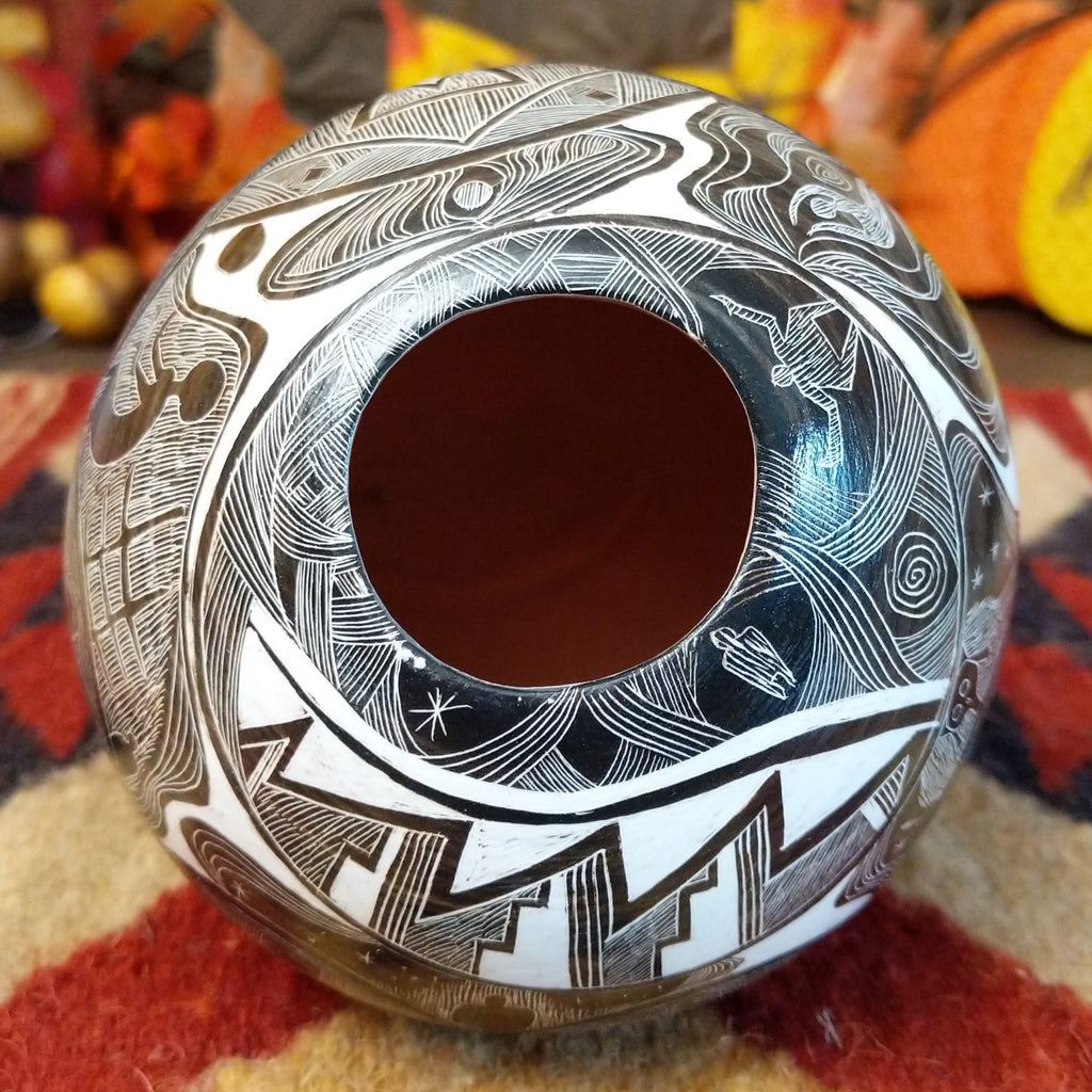 White clay with brown accents creating a pottery piece with intricately carved designs all along the surface and a smooth lip on the pot.