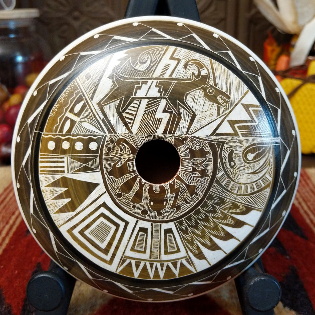 White clay with brown accents creating a pottery piece with a mesa, animals, people, and creative designs.