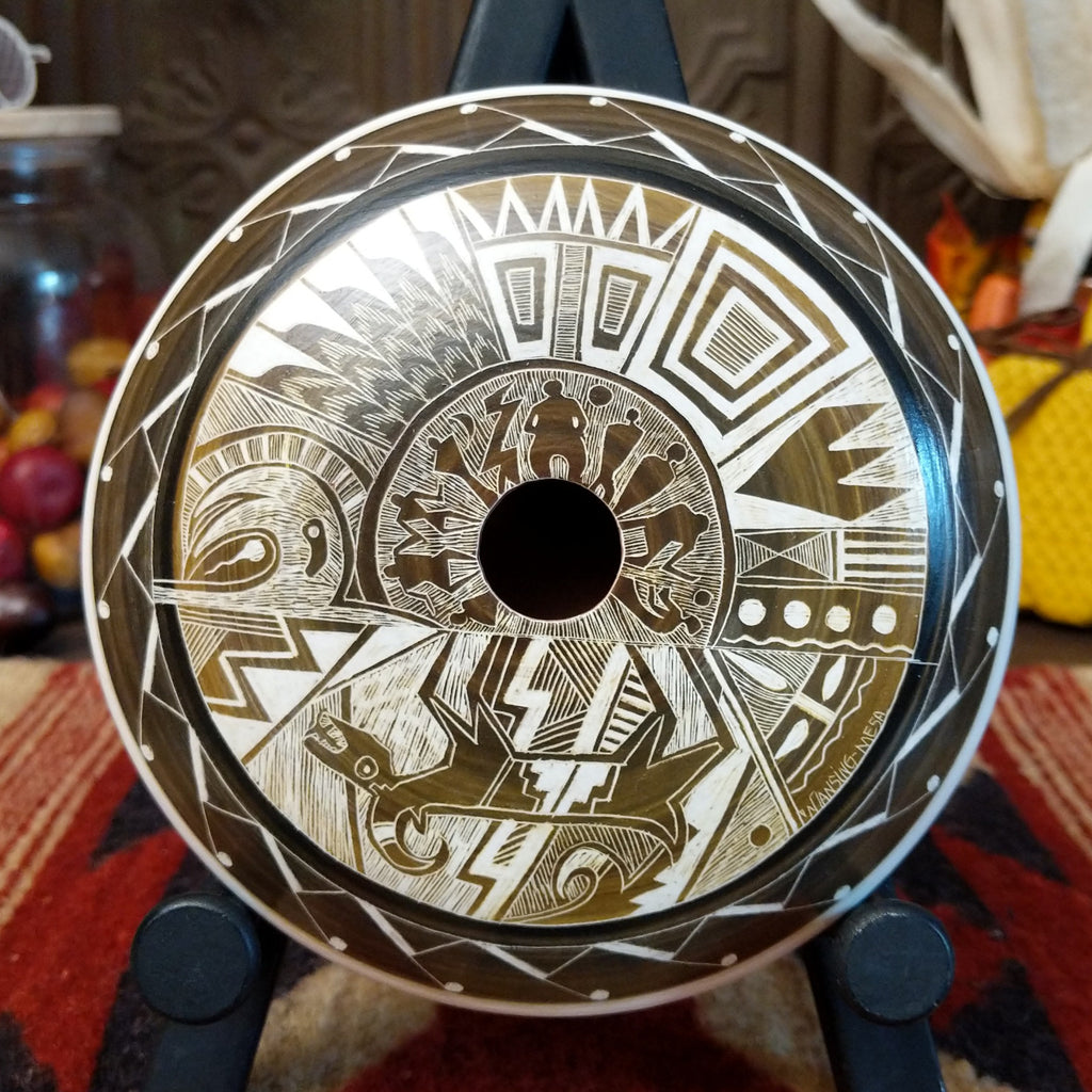 White clay with brown accents creating a pottery piece with a mesa, animals, people, and creative designs.