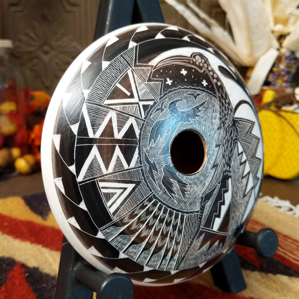 White clay creating a pottery piece with black and brown accents, etched with depictions of birds, landscapes, and unique patterns.