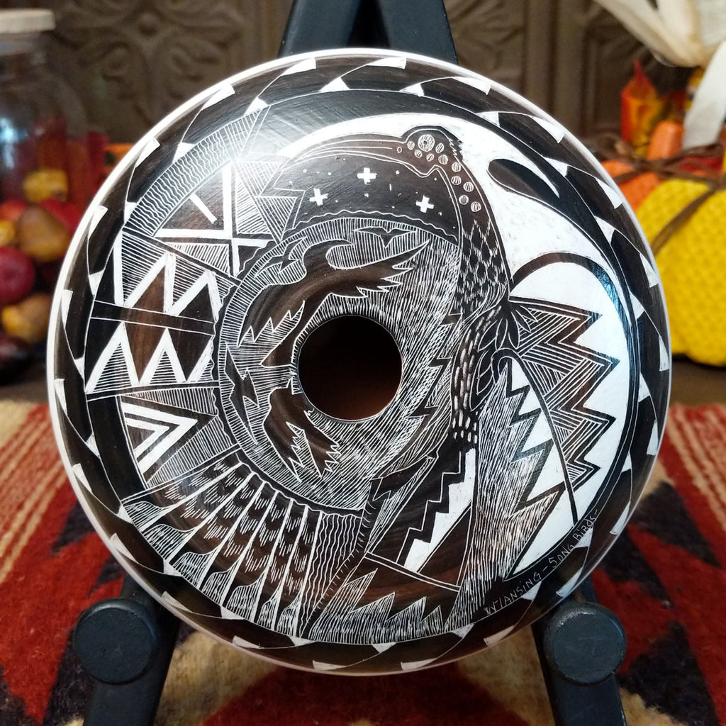 White clay creating a pottery piece with black and brown accents, etched with depictions of birds, landscapes, and unique patterns.