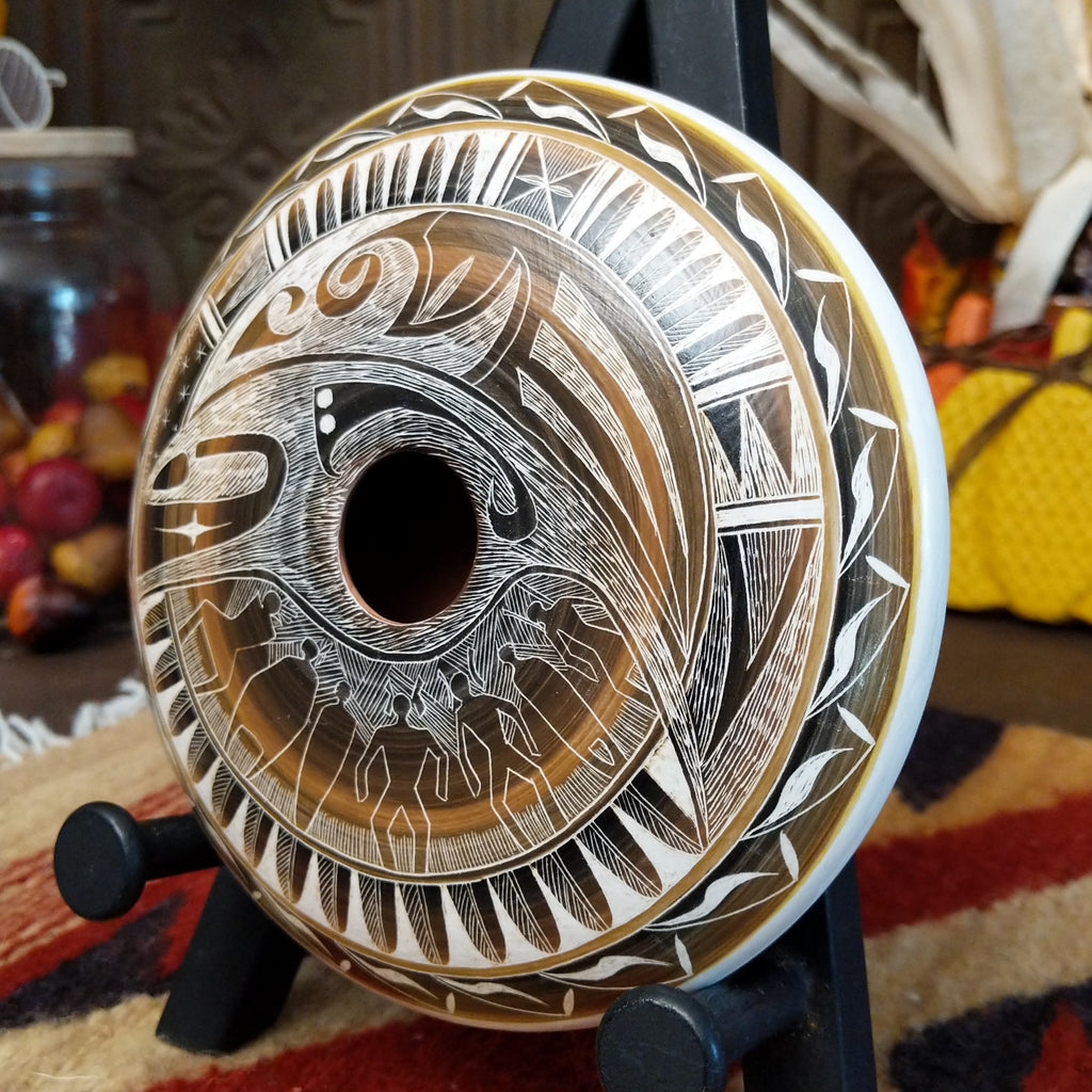 White clay pottery piece with warm tones, carved with depictions of people. wind, stars, and detailed patterns.