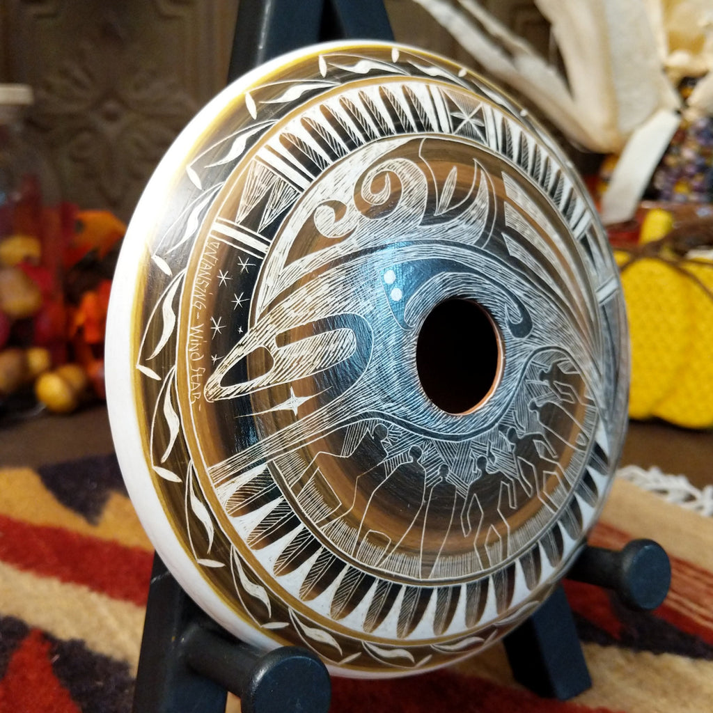 White clay pottery piece with warm tones, carved with depictions of people. wind, stars, and detailed patterns.