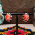 Warm Water Spiny Oyster Shell Oval Earrings set by Priscilla Smith features polished red-orange oval shell cabochons with natural color variations, set in silver with twisted rope-style borders.