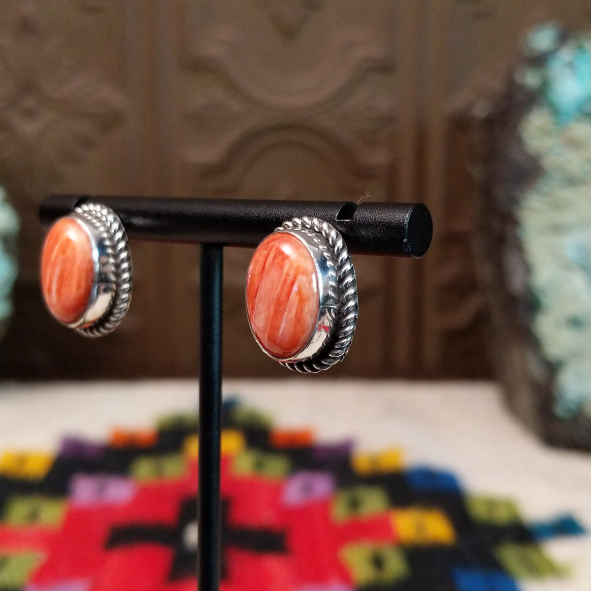 Warm Water Spiny Oyster Shell Oval Earrings by Priscilla Smith featuring polished coral-orange oval shell cabochons with natural color variations, set in silver with twisted rope-style borders; side view.