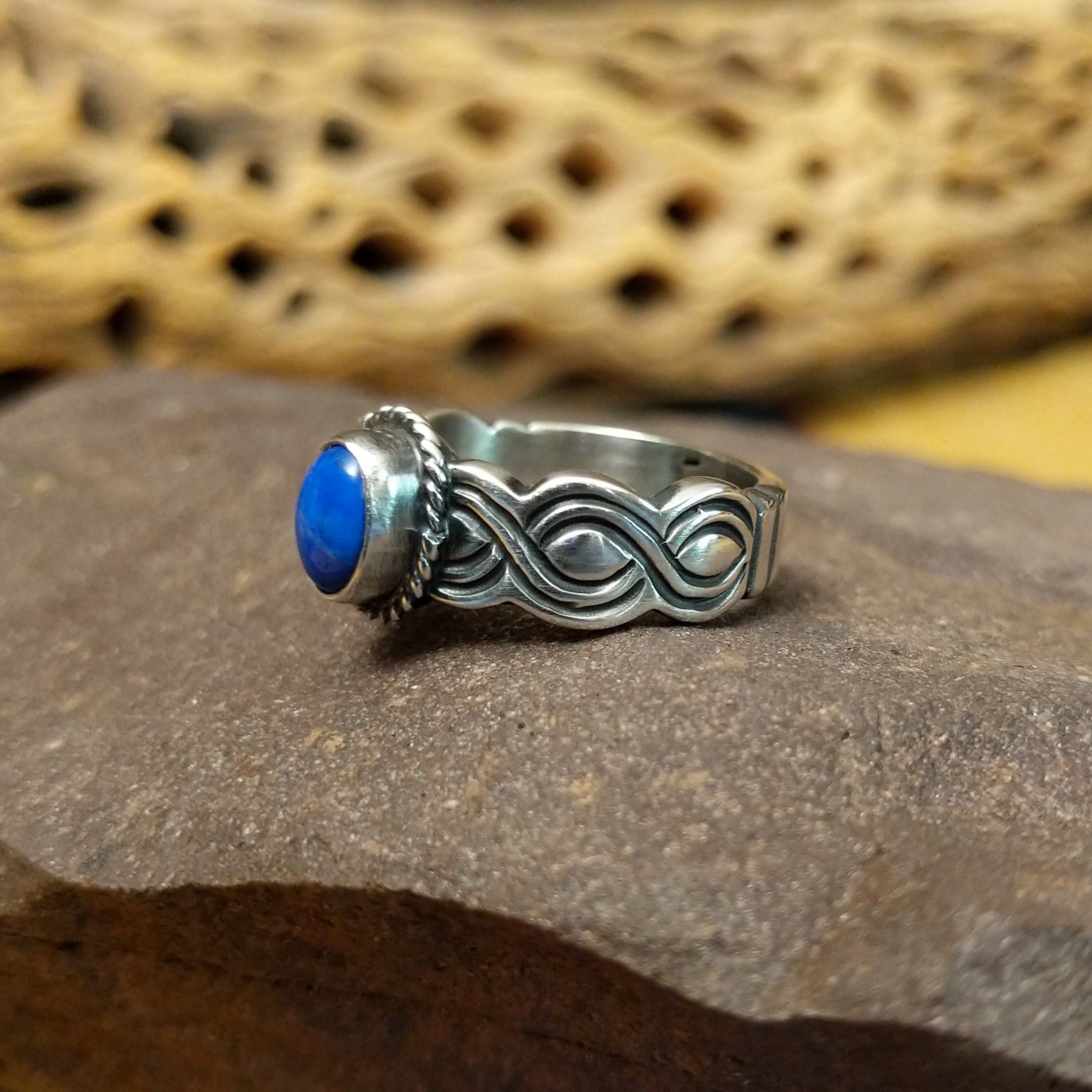 Lapis ring with weaving band by Raymond Coriz, featuring a deep blue lapis stone with natural pyrite flecks set in a handcrafted sterling silver woven band.  Side view.