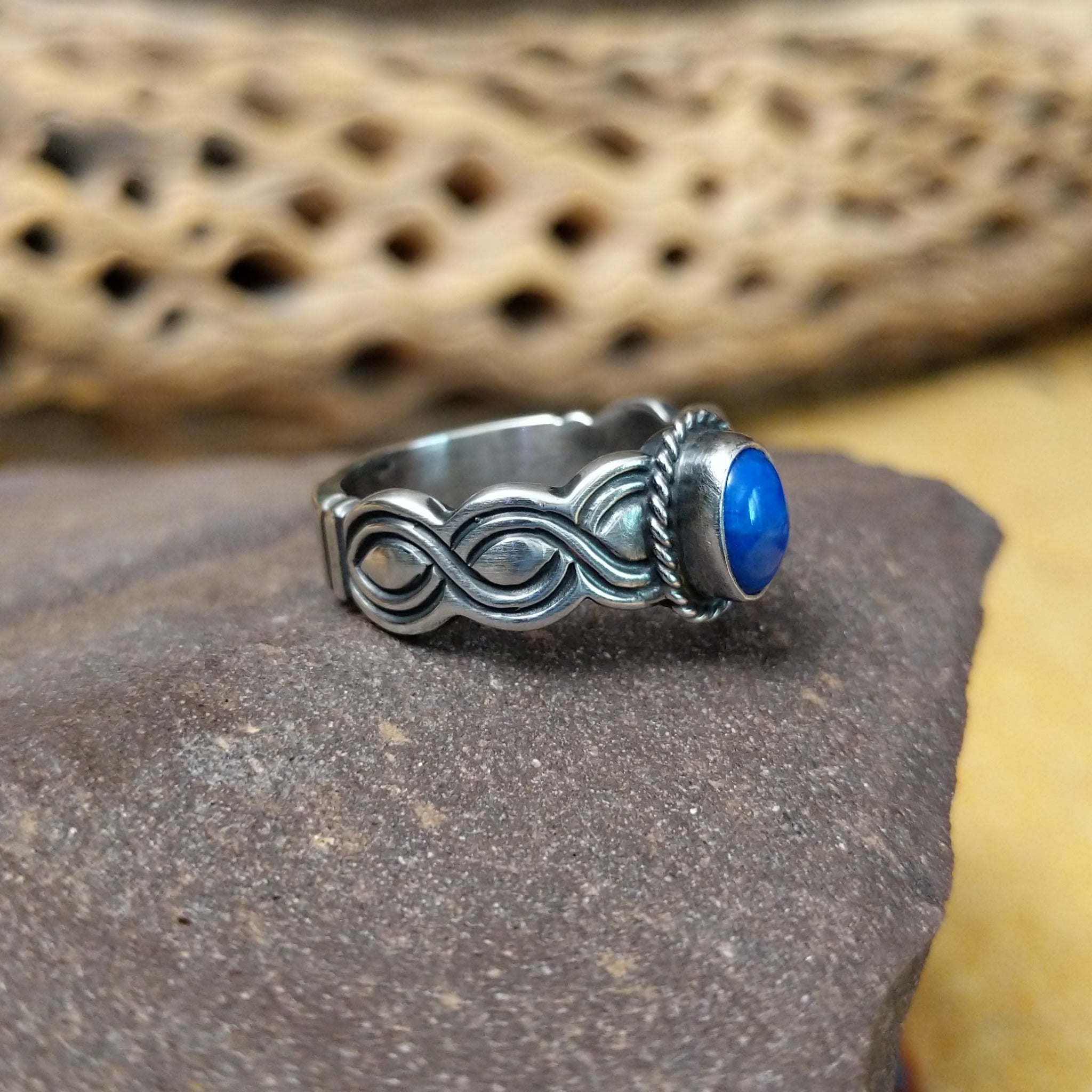 Lapis ring with weaving band by Raymond Coriz, featuring a deep blue lapis stone with natural pyrite flecks set in a handcrafted sterling silver woven band.  Side view.
