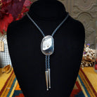 A Sterling Silver bolo tie necklace with a polished oval White Buffalo stone and braided cord, displayed on a black velvet jewelry bust.