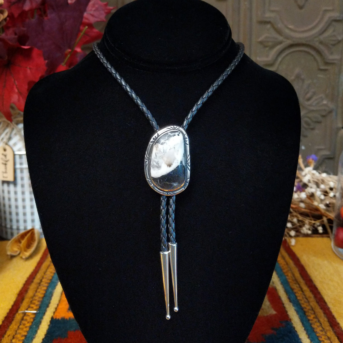 A Sterling Silver bolo tie necklace with a polished oval White Buffalo stone and braided cord, displayed on a black velvet jewelry bust.