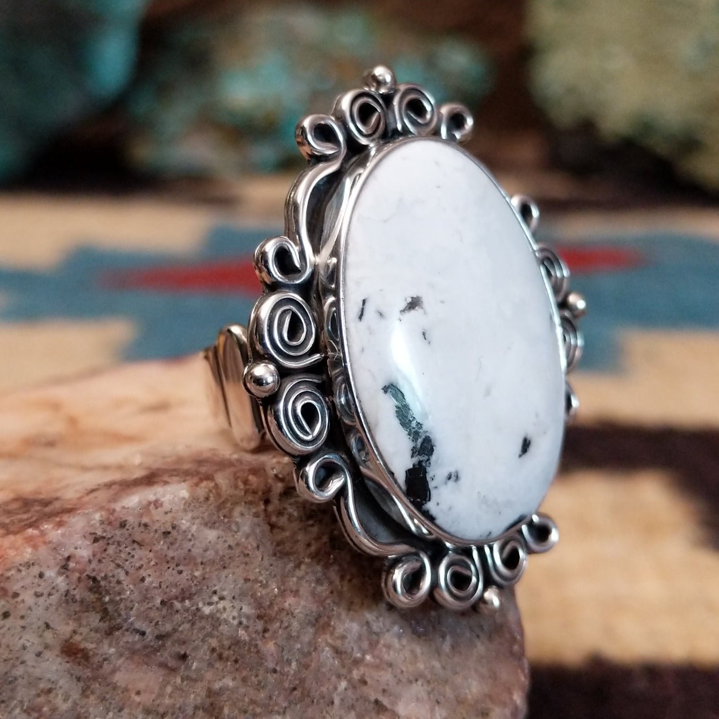 Sterling silver ring features white buffalo set in oval bezel with filigree pattern.