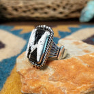 Handcrafted sterling silver White Buffalo ring by Alfred Martinez, featuring a rectangular White Buffalo gemstone with a twisted rope border and silver bead accents; side view.